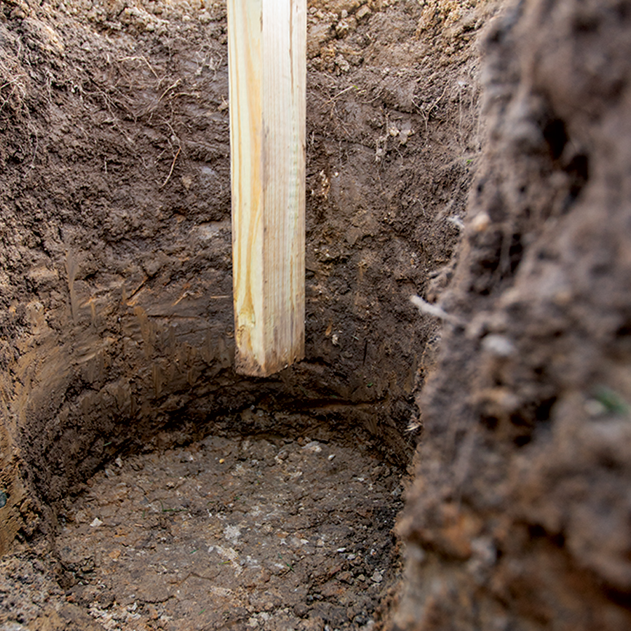 A 2x4 being used to compact dirt at the bottom of a hole.